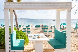 A beachside seating area with white tables and teal cushions, overlooking the sea. - La Playa Orient Bay (Orient Bay)