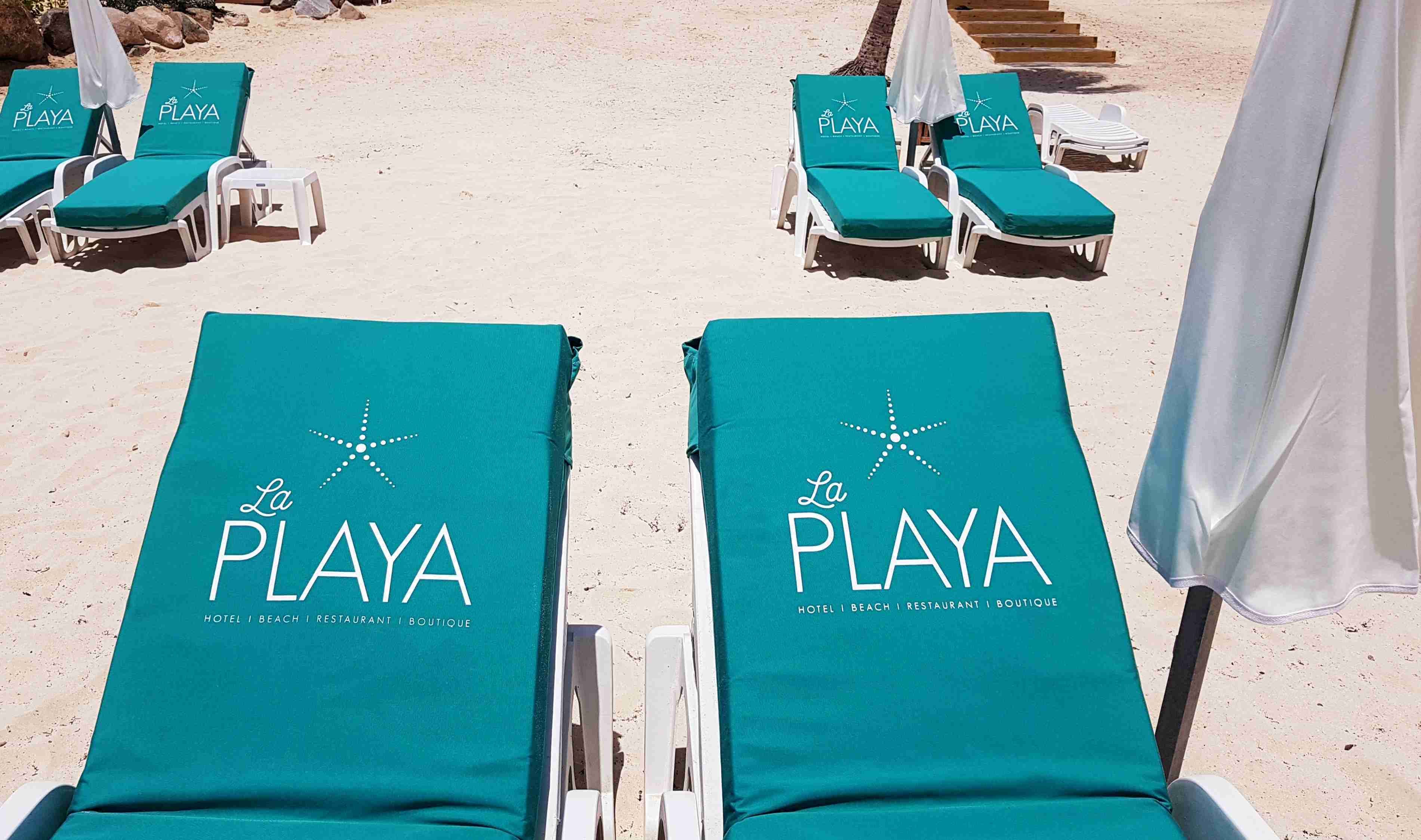 Dos filas de sillas de playa con cojines verdes y estructura blanca, con la etiqueta "La Playa" en los respaldos.
