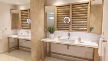 A modern bathroom with two sinks, wooden slatted mirrors, and a potted plant.