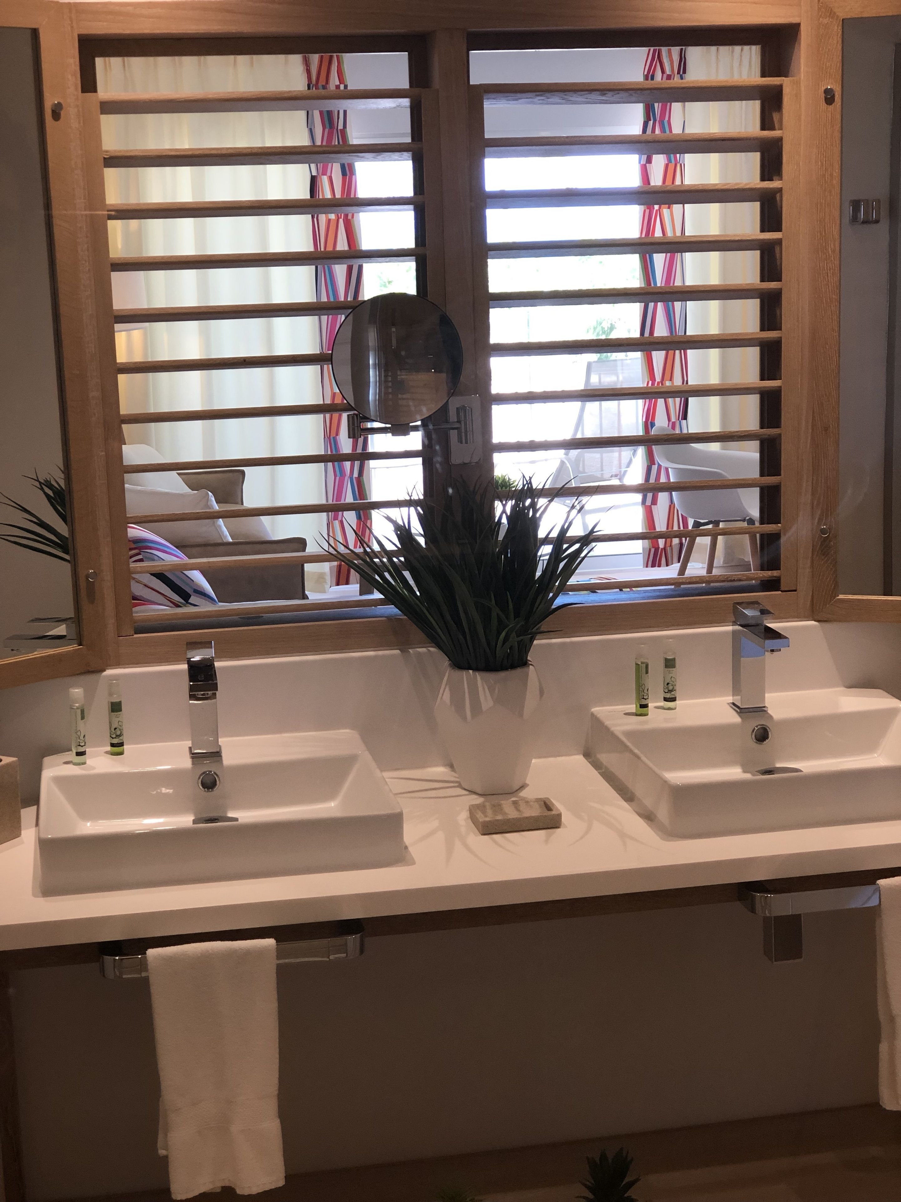 Un baño con dos lavamanos, un espejo y una ventana con persianas.
