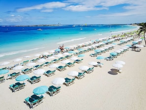 A beach with rows of sun loungers and umbrellas, a clear blue sea, and a distant rocky shoreline. - La Playa Orient Bay (Orient Bay)