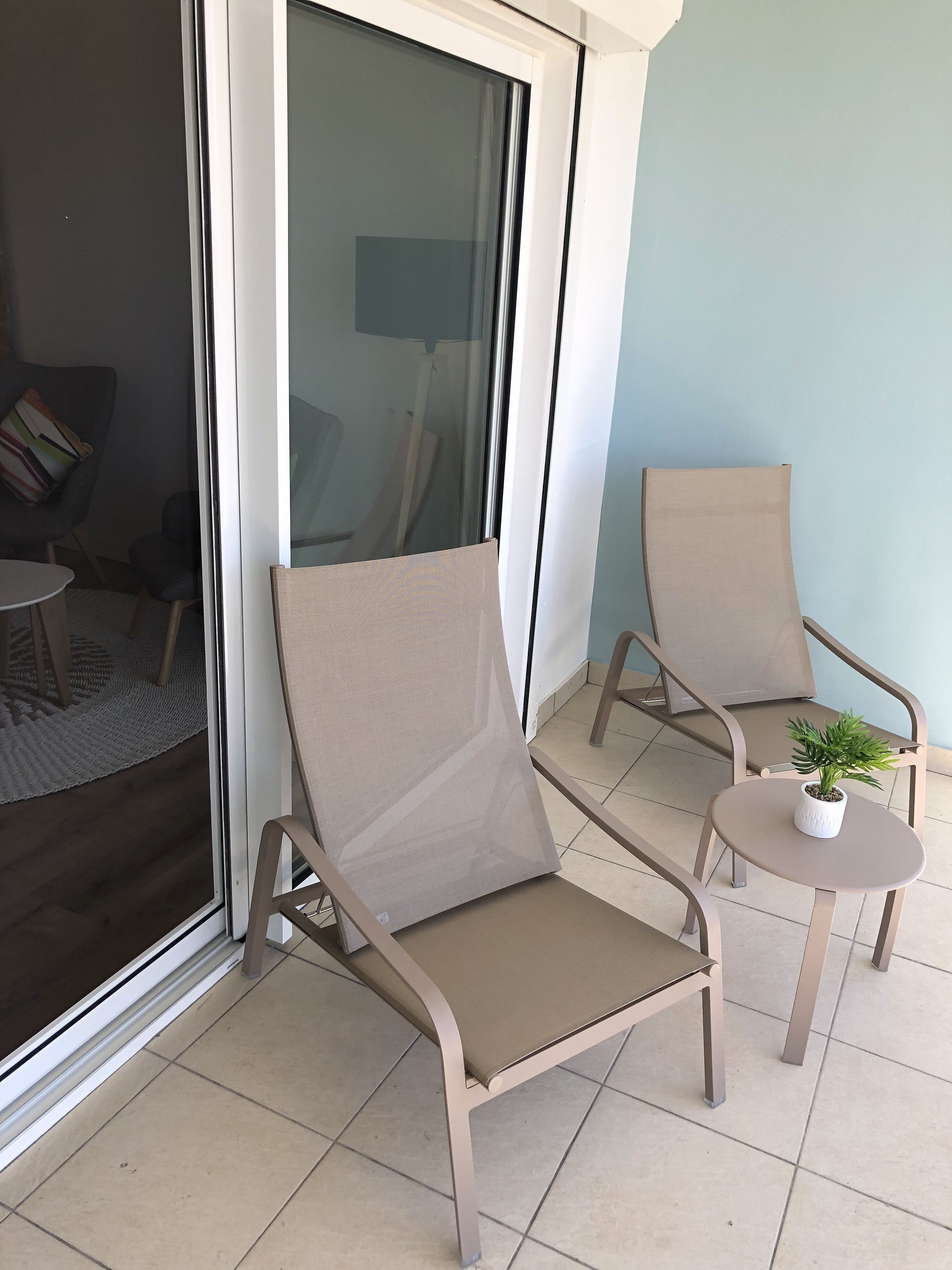 Un balcón con dos sillas color beige y una mesa pequeña con una planta en maceta.