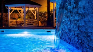 Una piscina con una cascada, un pabellón y un muro de piedra.