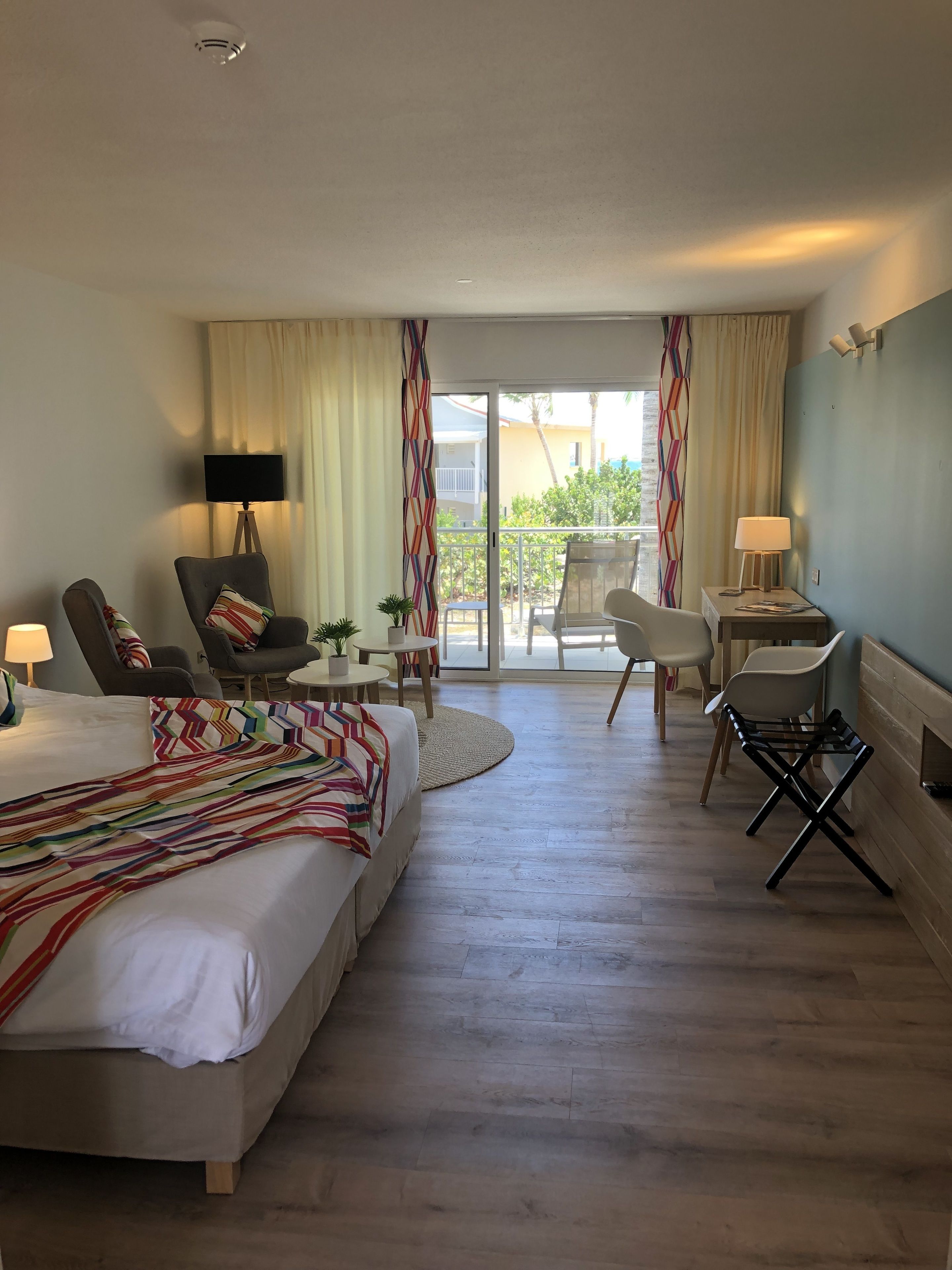 Una camera d'albergo con un letto, due poltrone, un tavolino, una TV e un balcone con tende.