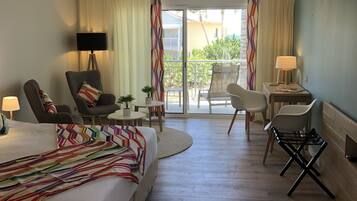 Una camera d'albergo con un letto, due poltrone, un tavolino, una TV e un balcone con tende.