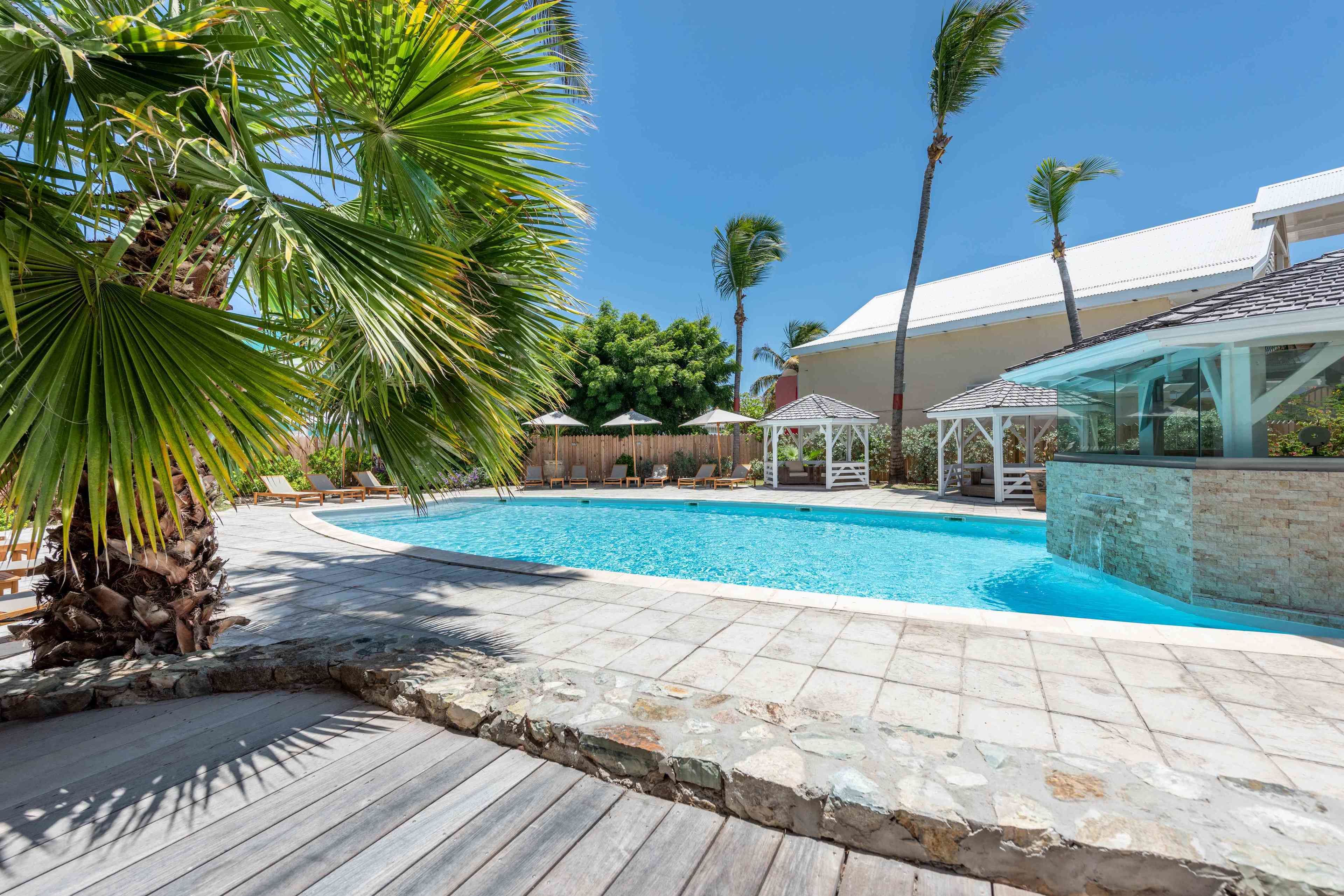 A swimming pool with a wooden deck, palm trees, and a gazebo.