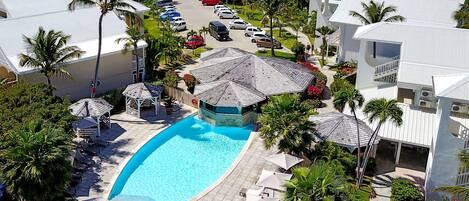 A resort with a swimming pool, palm trees, and a parking area.