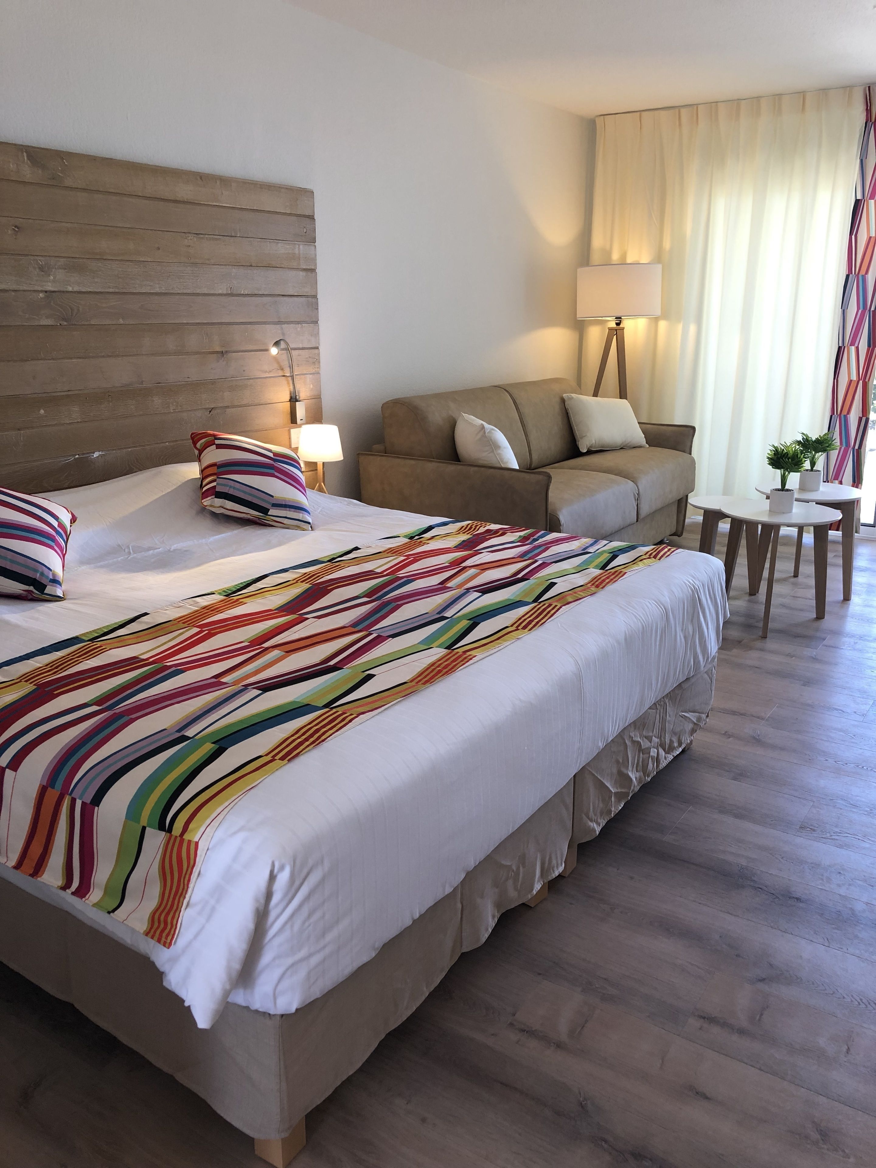 Quarto de hotel com uma cama grande, um sofá, uma mesinha e uma luminária.