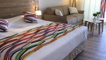 Quarto de hotel com uma cama grande, um sofá, uma mesinha e uma luminária.