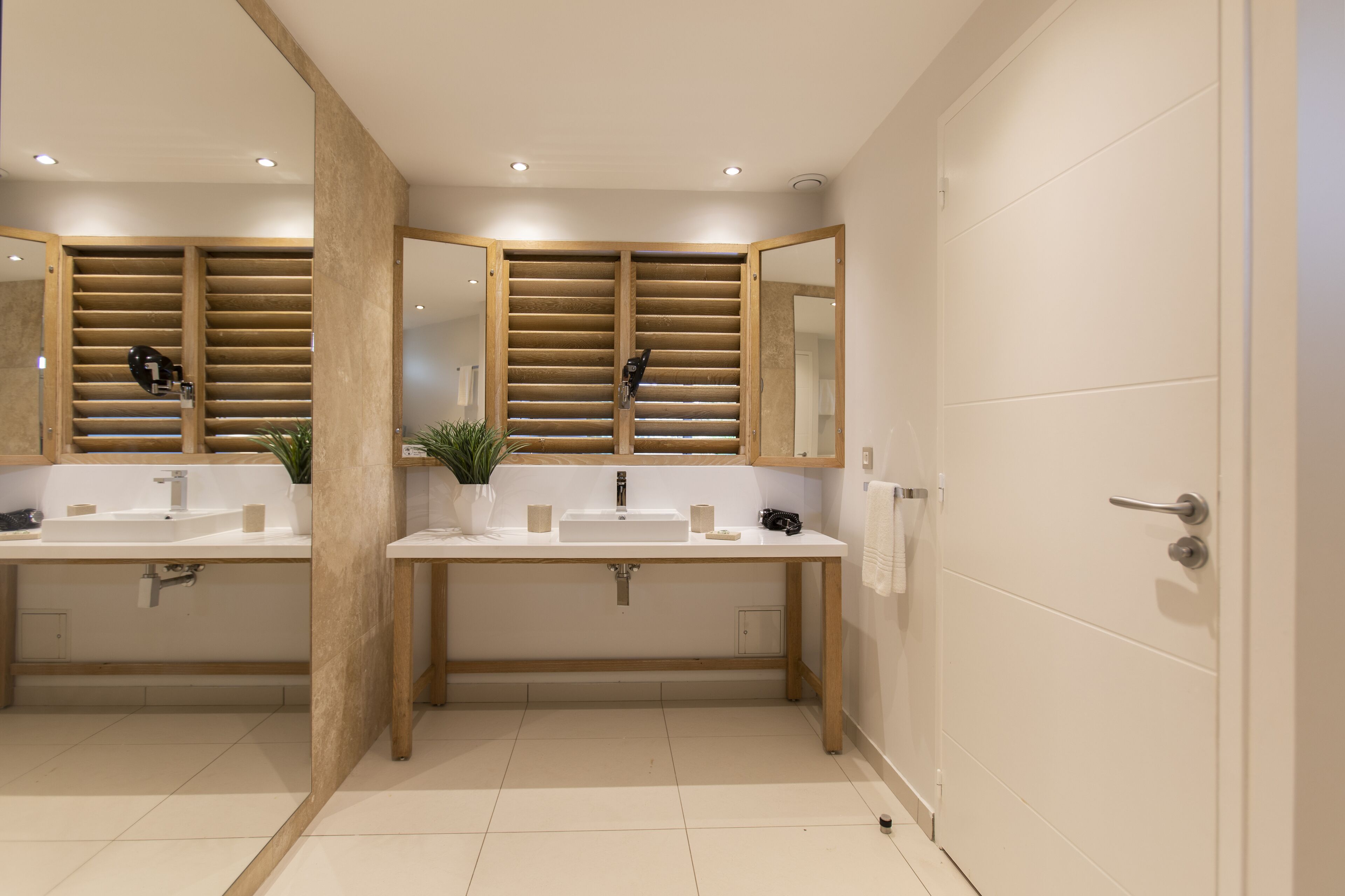 A modern bathroom with two sinks, wooden slatted shower doors, and a large mirror.