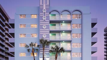 Un hotel de varios pisos con balcones, un elemento vertical central y palmeras en primer plano.