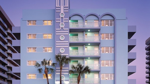 A multi-story hotel with balconies, a central vertical design element, and palm trees in front. - Solara Surfside (Surfside)