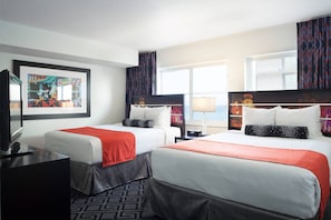 A hotel room with two beds, a desk, a TV, and a large window with curtains. - Solara Surfside (Surfside)