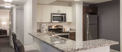 A modern kitchen with a granite countertop, stainless steel appliances, and white cabinetry.