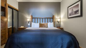 A large bed with a quilted blue cover, wooden headboard, two bedside lamps, and a framed picture on the wall.