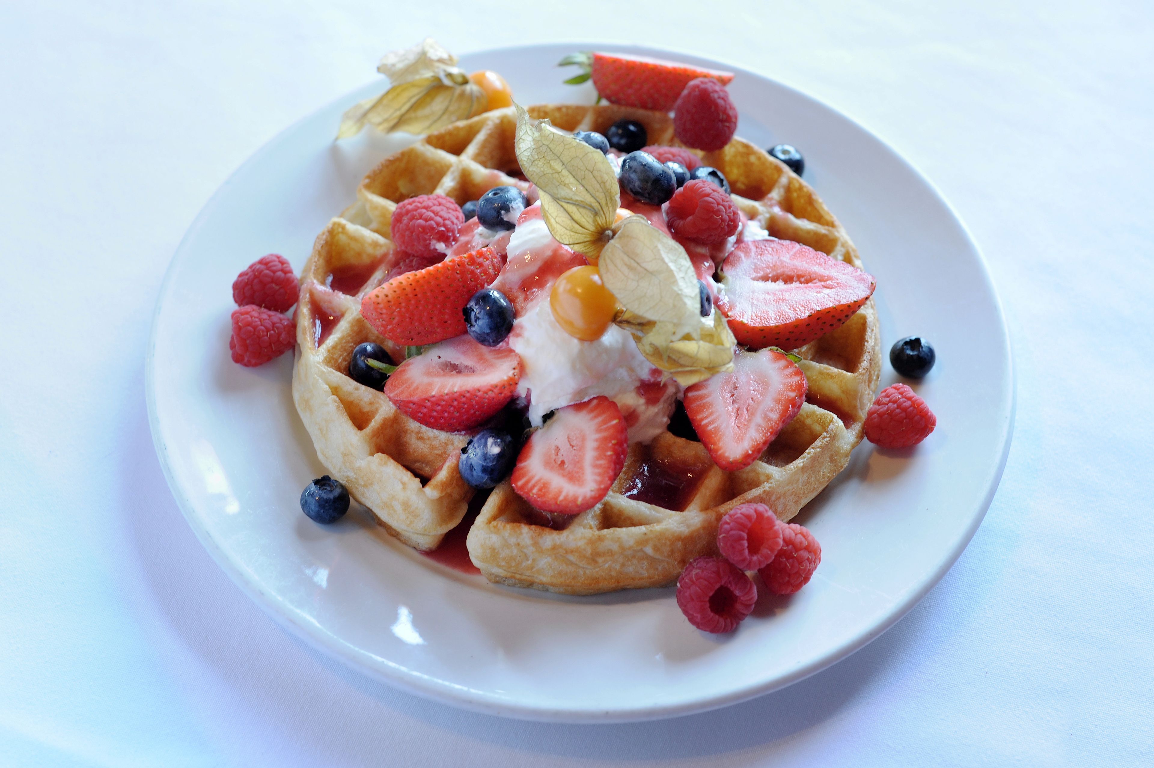 A plate of waffles topped with strawberries, blueberries, raspberries, and a dollop of cream.