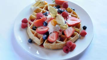 A plate of waffles topped with strawberries, blueberries, raspberries, and a dollop of cream.
