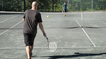 A tennis court with a net, a player in a black shirt and shorts, and another player in the background.