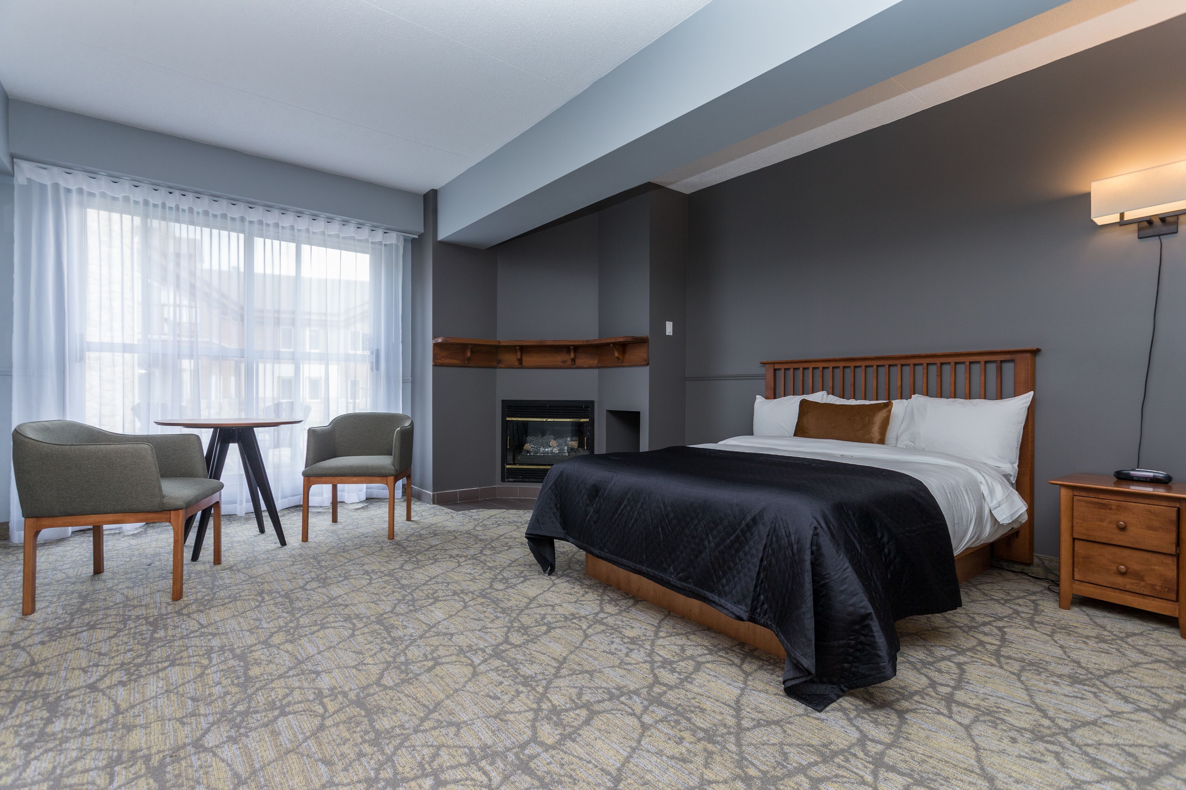 Habitación de hotel con una cama grande, dos sillones, una mesita, una chimenea y una mesita de noche.