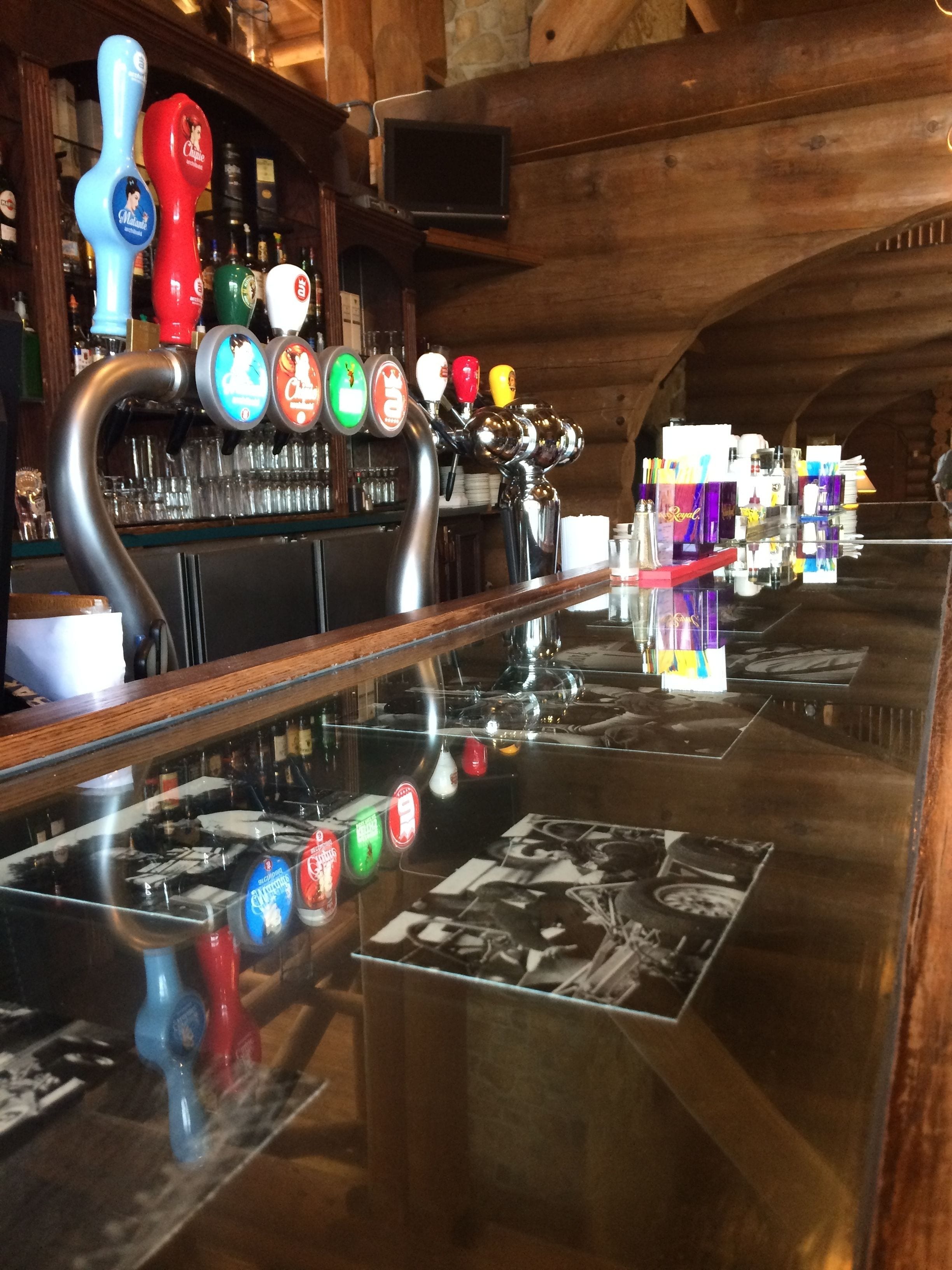 Um bar com várias torneiras de cerveja, uma televisão fixada na parede e uma variedade de garrafas e copos nas prateleiras.