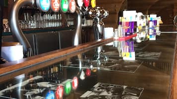 Um bar com várias torneiras de cerveja, uma televisão fixada na parede e uma variedade de garrafas e copos nas prateleiras.