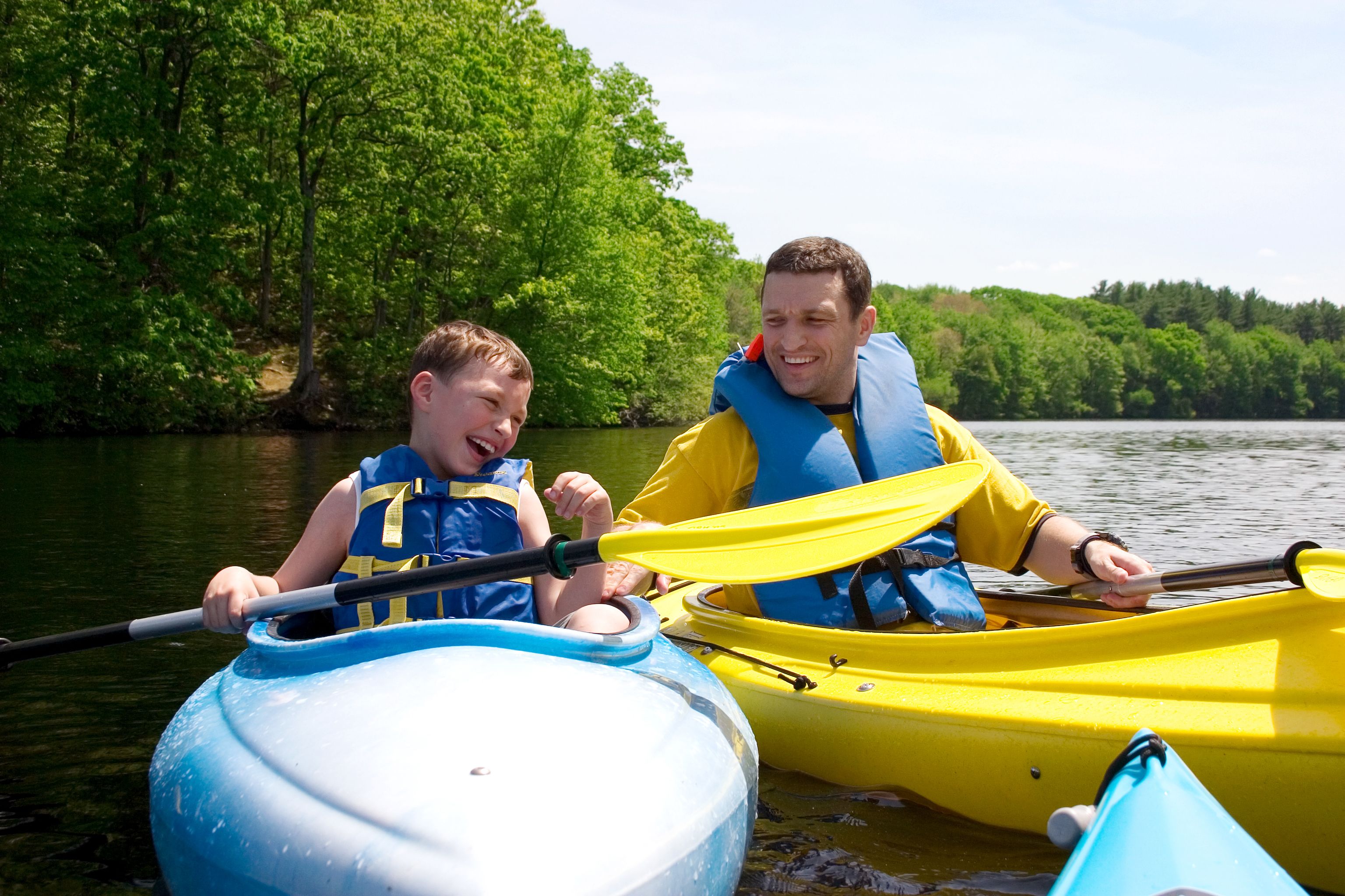 Two people in a yellow kayak on a calm river surrounded by lush greenery.