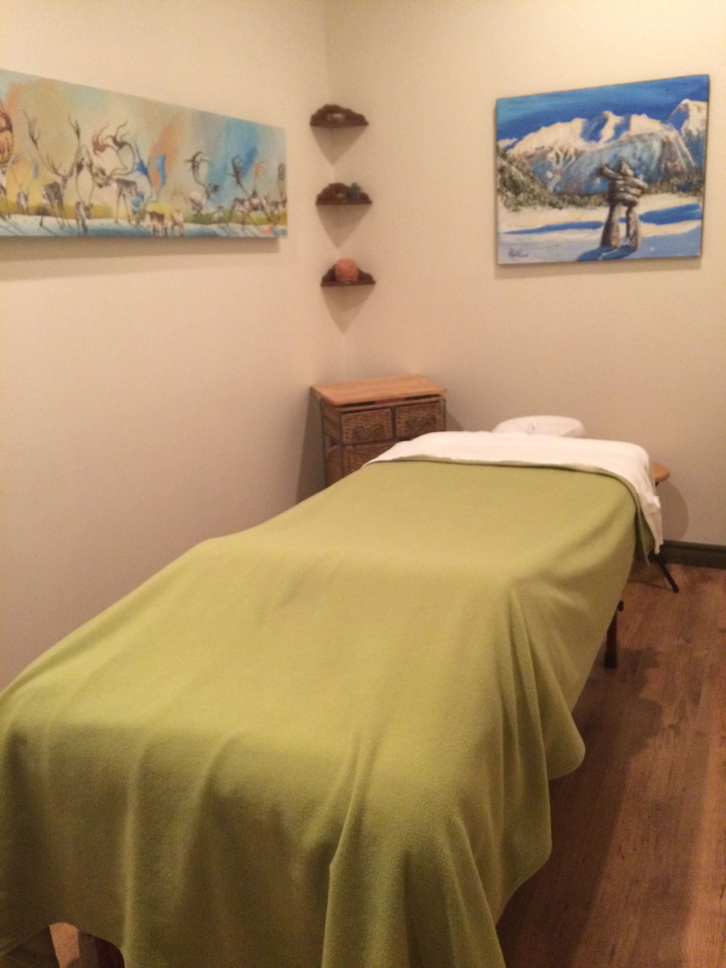 A room with a bed, a small wooden cabinet, and two paintings on the wall.