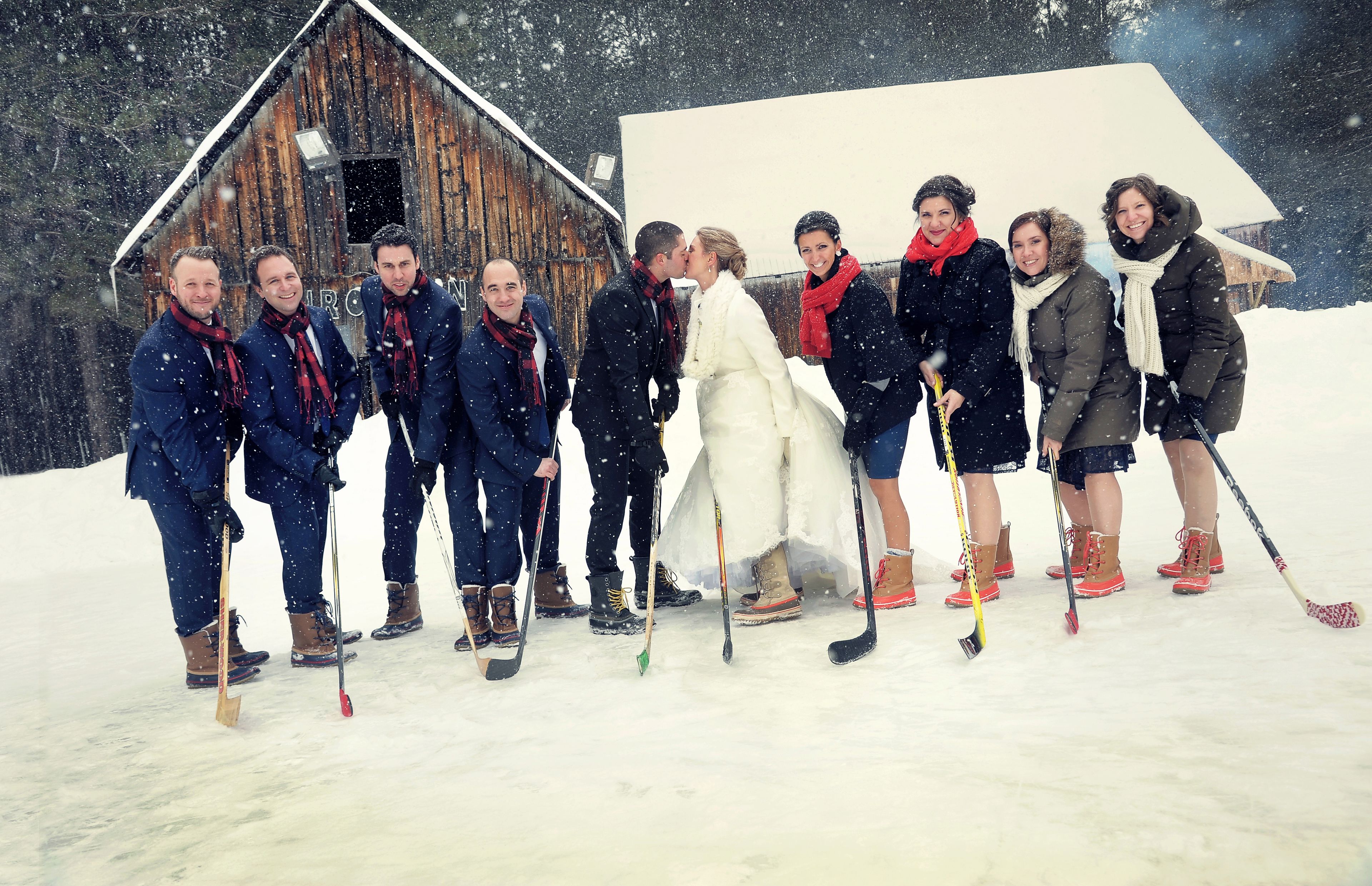 A group of people in winter sports attire standing in a snowy outdoor setting with a wooden structure in the background.