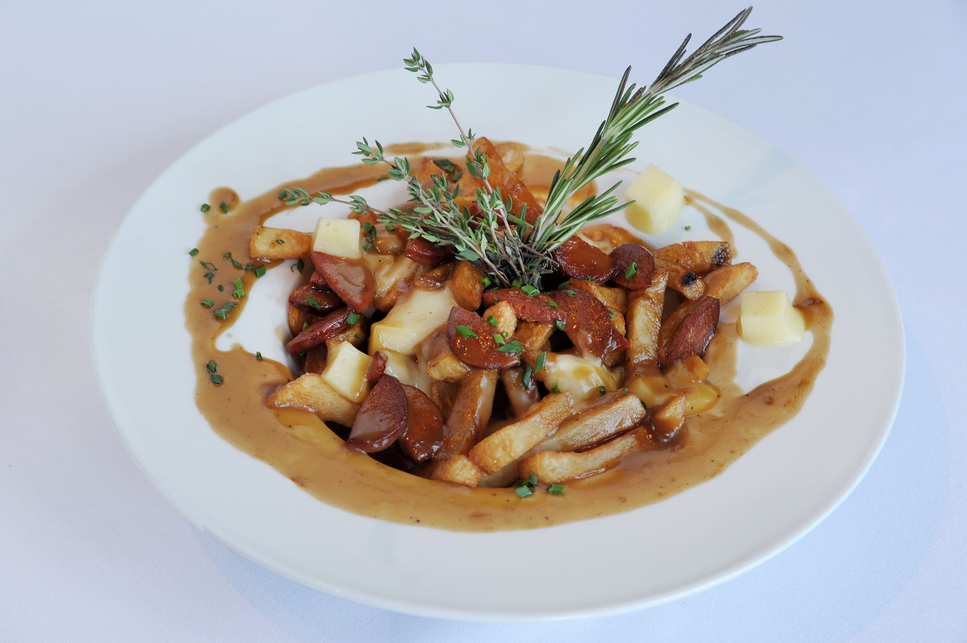 A plate of poutine with fries, cheese curds, and gravy, garnished with herbs.