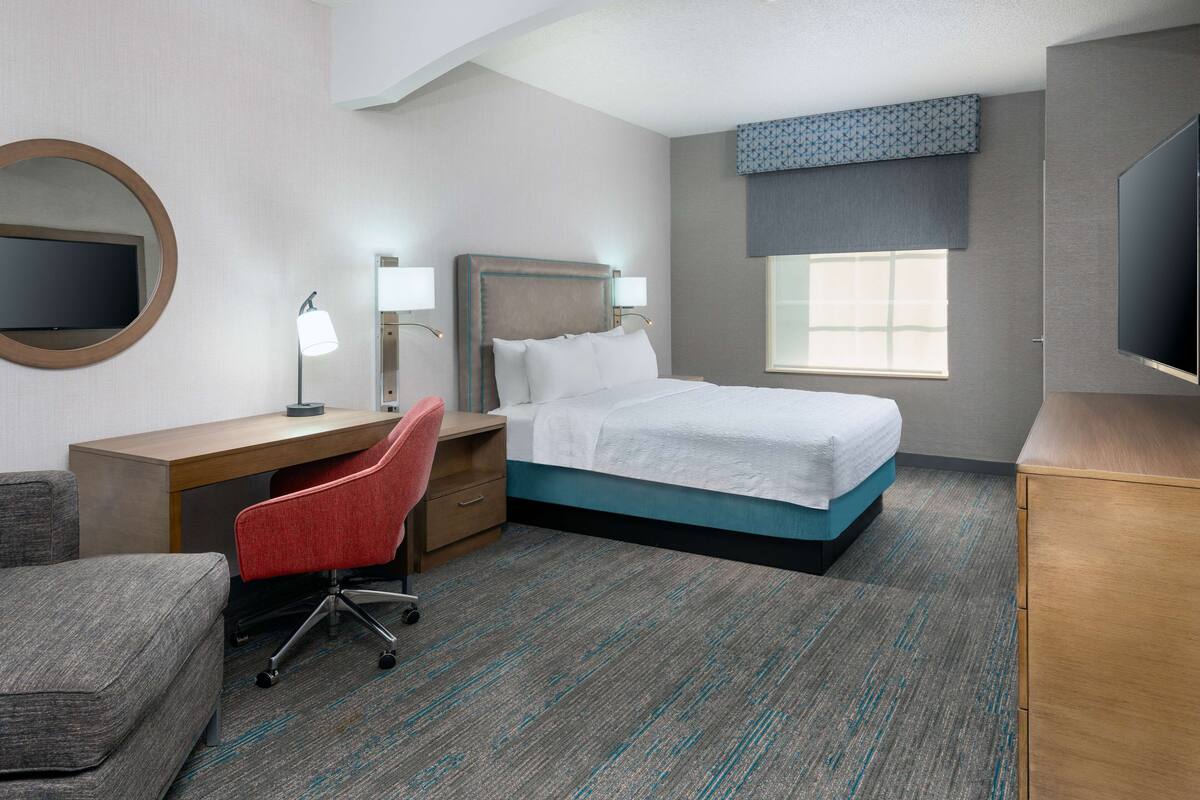 A hotel room with a bed, desk, chair, TV, and a window.