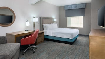 Una habitación de hotel con cama, escritorio, silla, televisor y ventana.