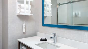 A modern bathroom with a white sink, chrome faucet, and a large mirror with a blue frame. There are shelves with towels and toiletries.