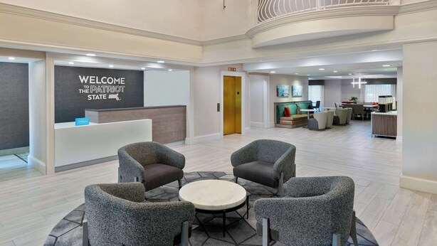 A spacious lobby with a reception desk, seating area, and a staircase leading to an upper level. - Hampton Inn Boston Bedford Burlington (Billerica)