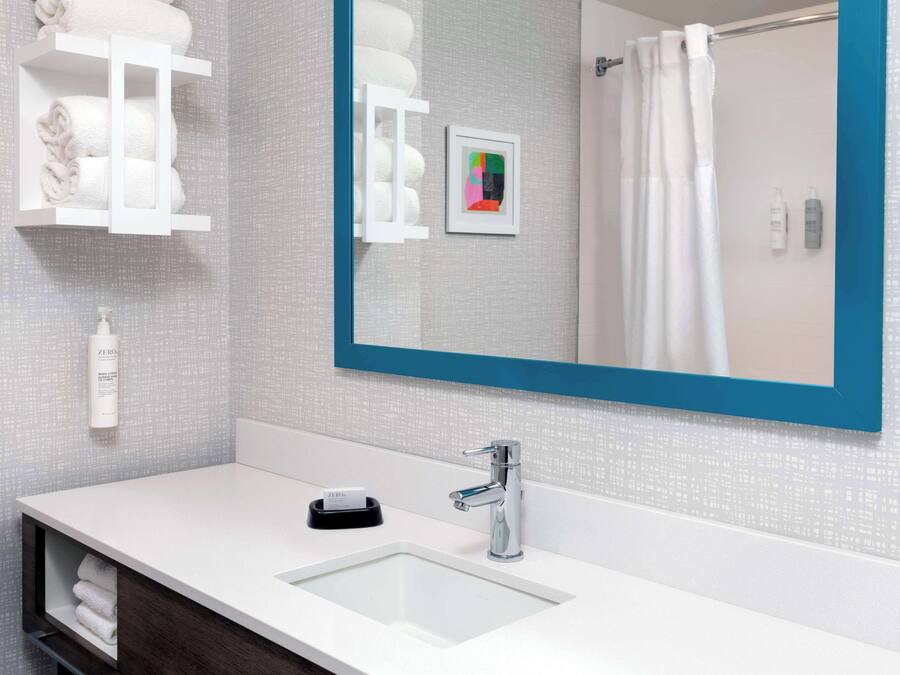 Un baño moderno con un lavamanos blanco, un espejo grande con marco azul y un perchero con toallas dobladas con esmero.