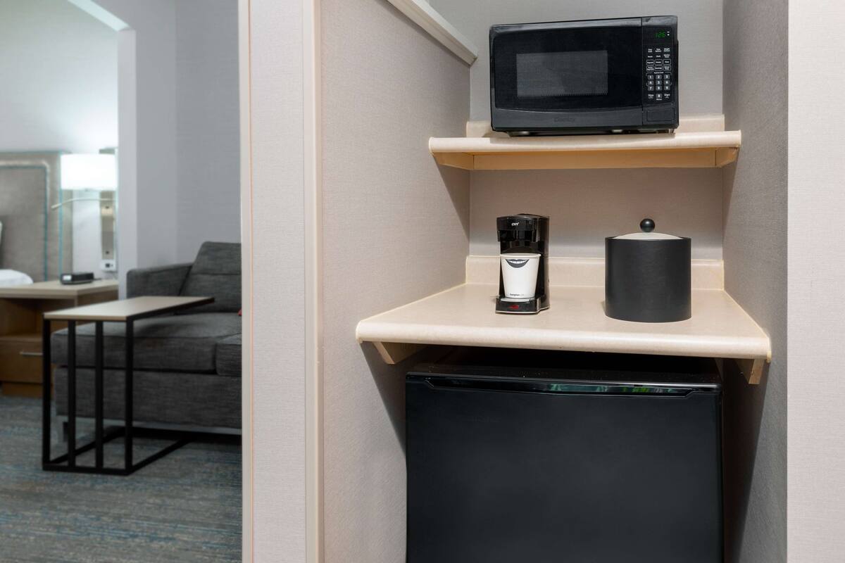 A compact kitchenette with a microwave, coffee maker, and a trash bin.