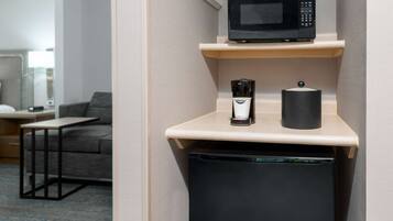 A compact kitchenette with a microwave, coffee maker, and a trash bin.