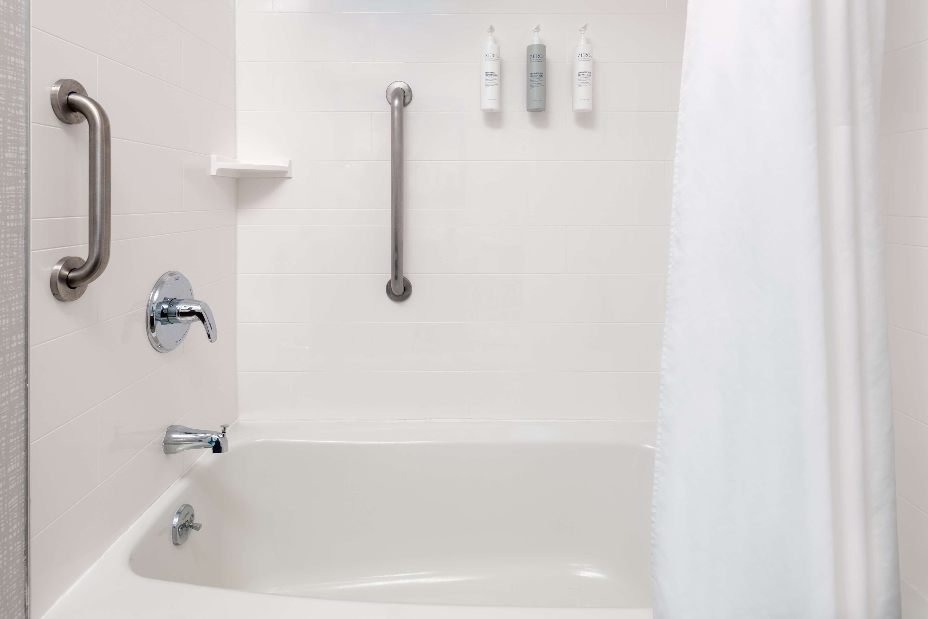 Un baño con bañera, barras de apoyo y artículos de aseo en la pared.