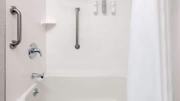 Un baño con bañera, barras de apoyo y artículos de aseo en la pared.