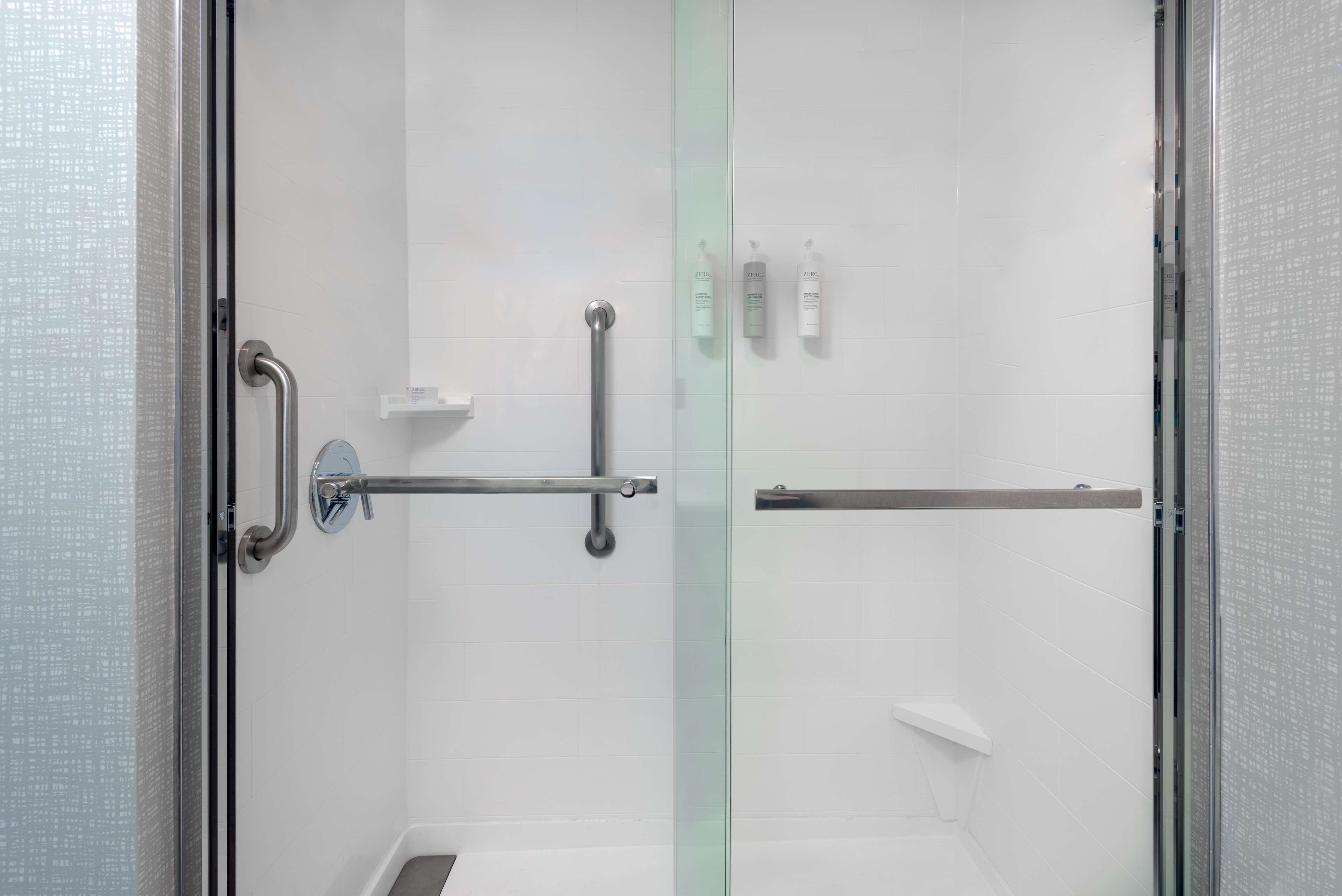 A modern shower with glass doors, a handrail, and a shelf with toiletries.