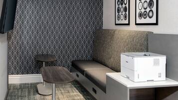 A compact room with a patterned wallpaper, a sofa, a small table, and a printer on a desk.