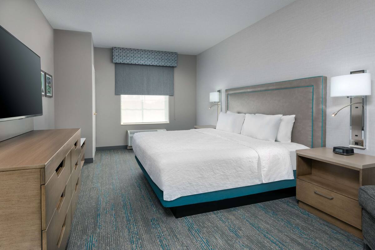 A hotel room with a large bed, bedside tables, a TV, and a window with a view.