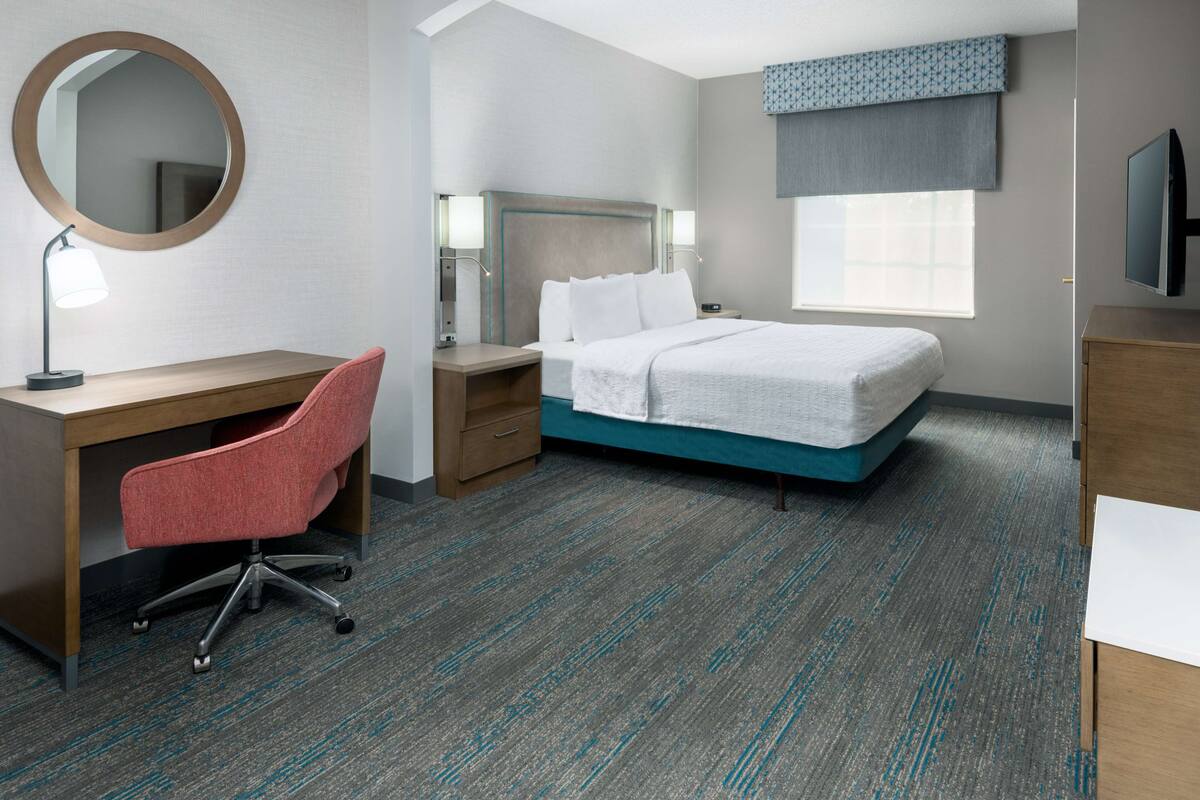A hotel room with a bed, desk, chair, and a large mirror.