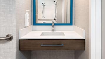 Une salle de bain avec un lavabo blanc, un miroir avec un cadre bleu, un porte-serviettes et une bouteille de shampoing.