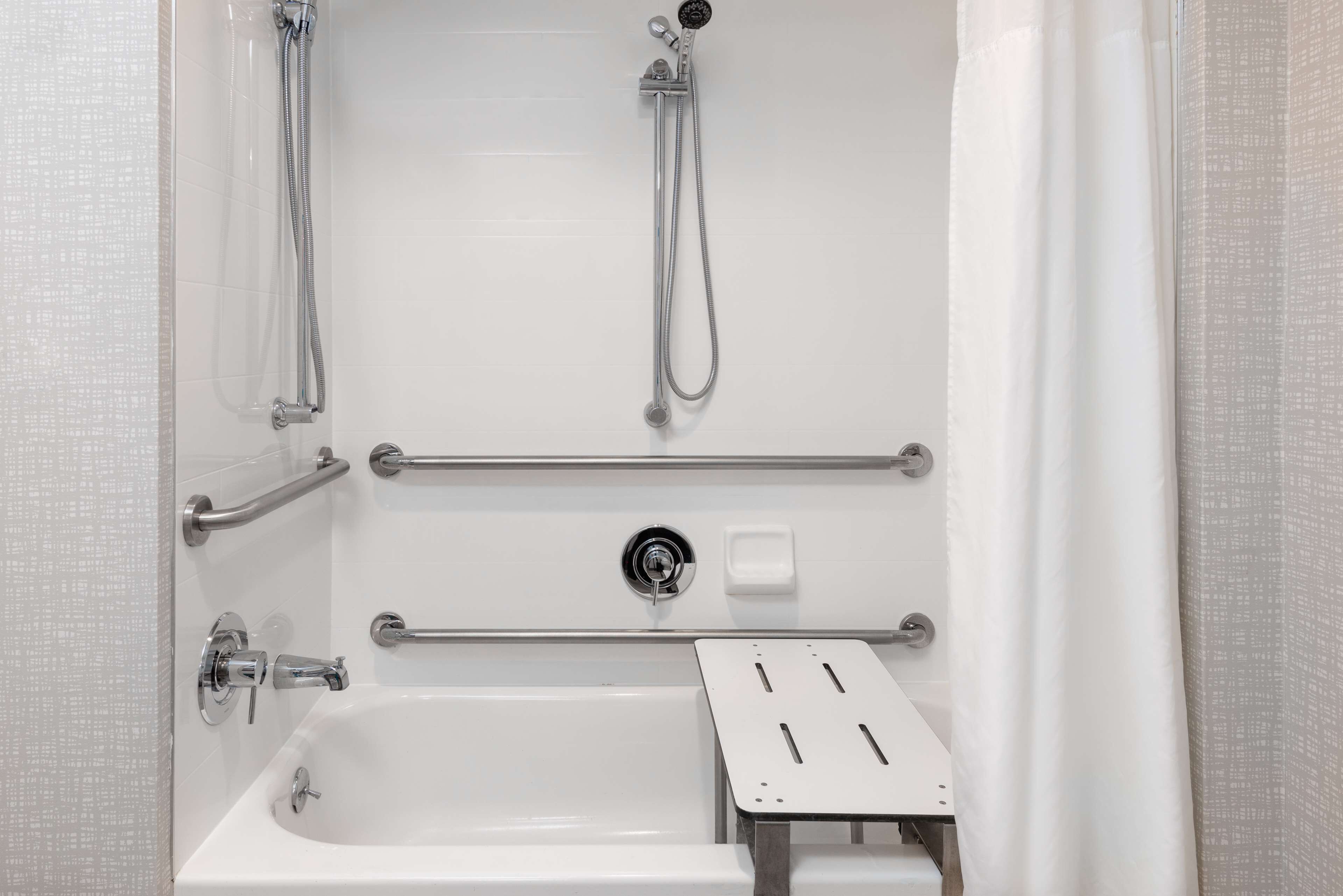 A modern bathroom with a bathtub, a shower with a handheld showerhead, and grab bars for safety.