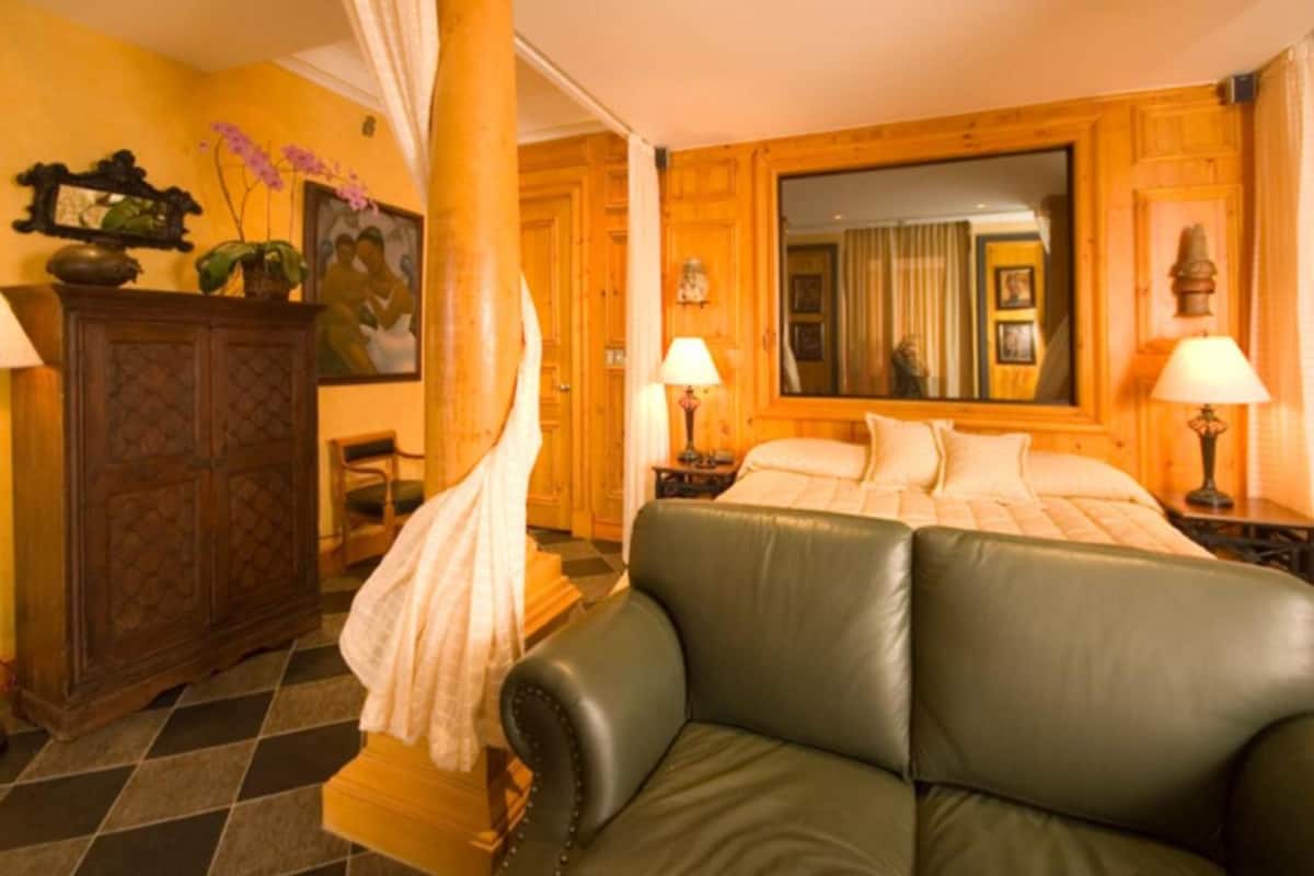 A room with a bed, a green leather sofa, a wooden cabinet, and a mirror on the wall.