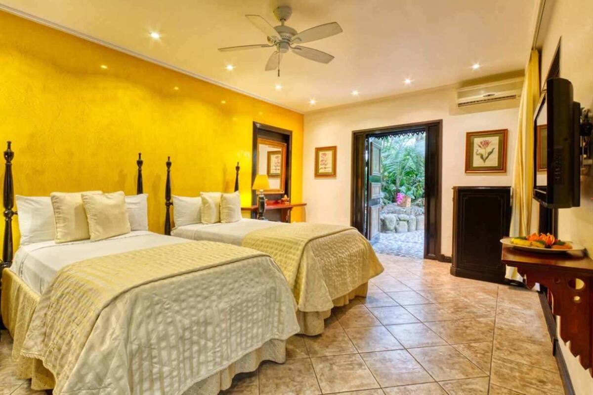 A hotel room with two beds, a ceiling fan, a TV, and a view of the outdoors.