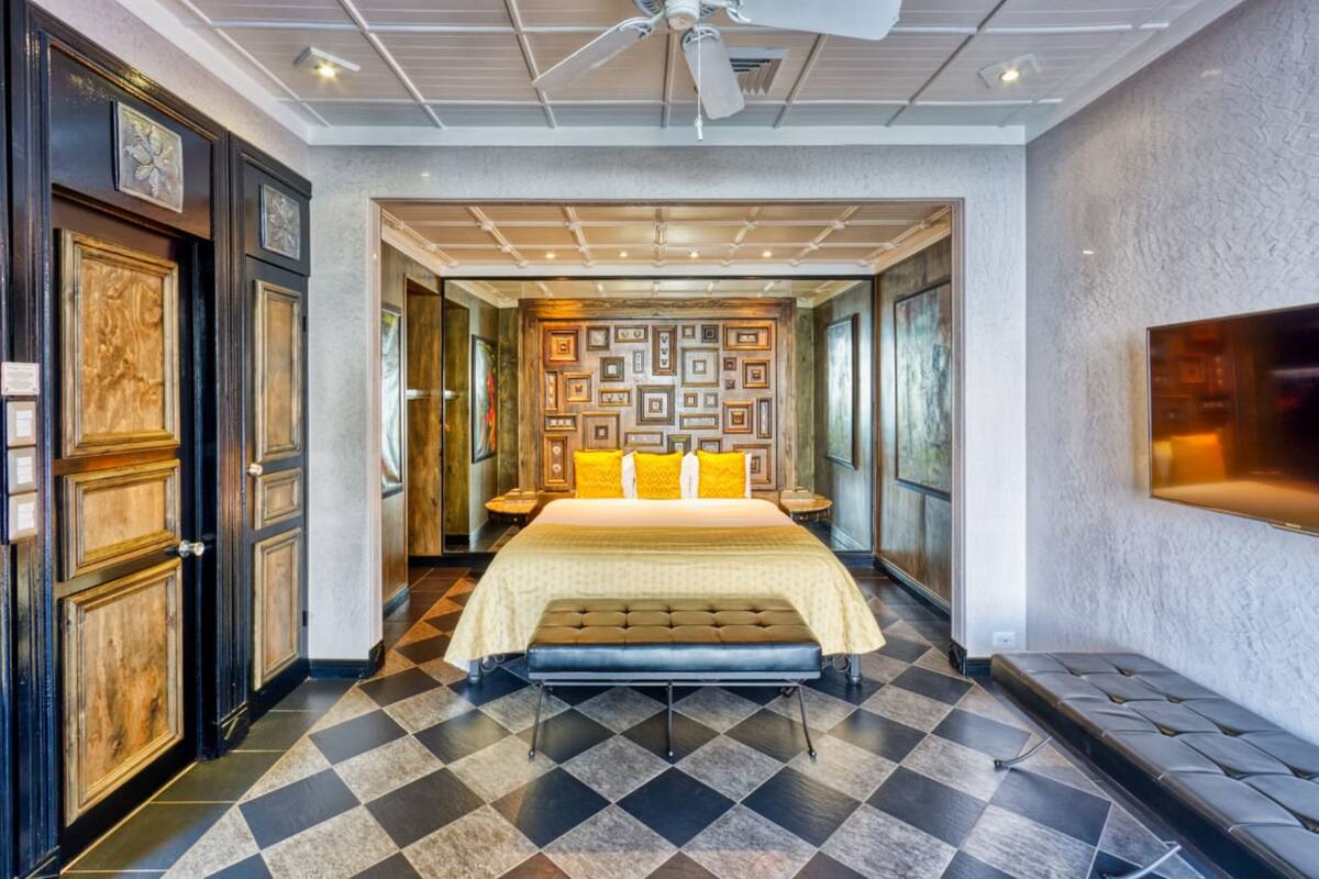 A hotel room with a large bed, a ceiling fan, a patterned wall, and a checkered floor.