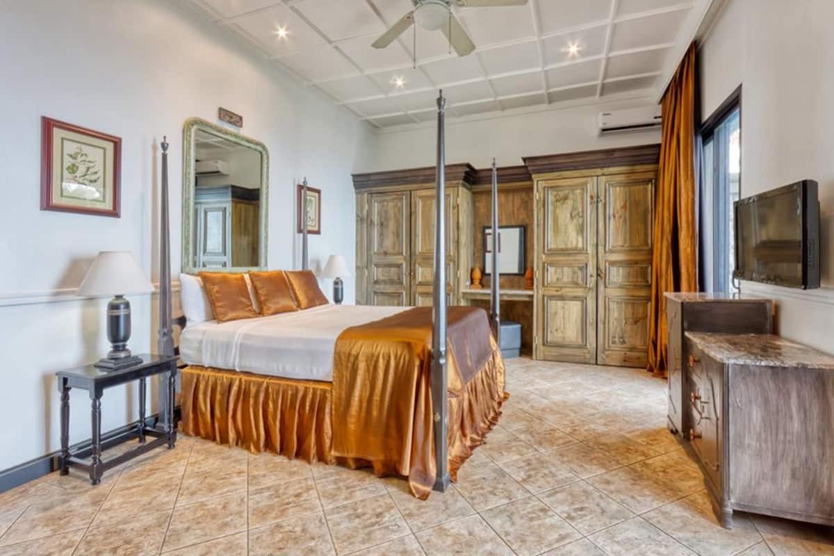 A spacious bedroom with a large bed, a ceiling fan, wooden cabinets, and a television.