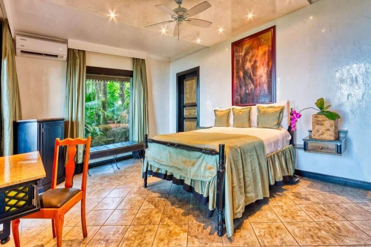 A bedroom with a bed, a desk, a chair, a ceiling fan, and a window with curtains.