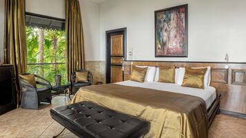 A hotel room with a large bed, a bench, wicker chairs, a TV, and a painting on the wall.